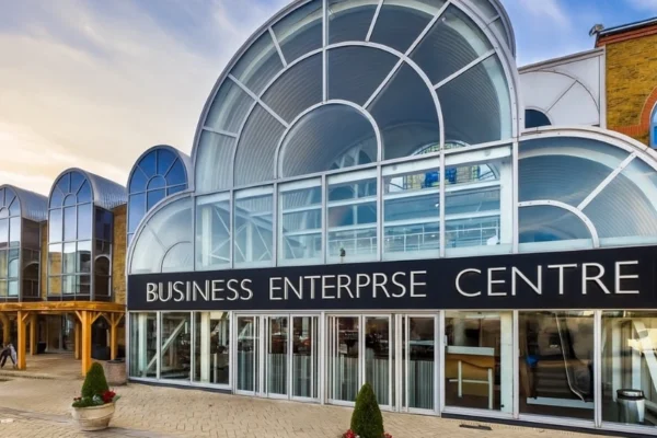 A modern business enterprise centre with entrepreneurs working at desks, attending a workshop, and networking in a collaborative space.