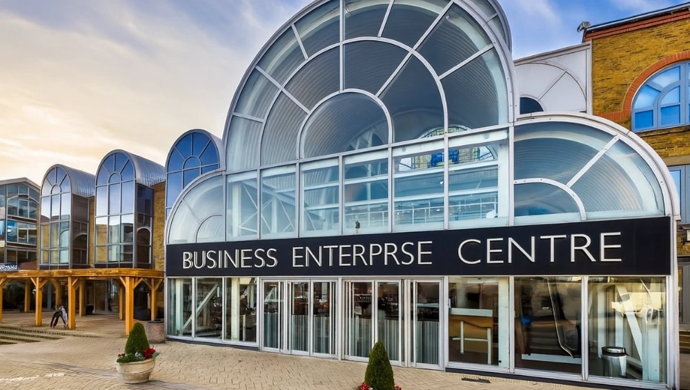 A modern business enterprise centre with entrepreneurs working at desks, attending a workshop, and networking in a collaborative space.