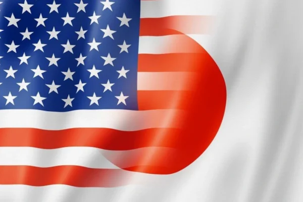 U.S and Japanese officials shaking hands after signing the US Japan Trade Agreement, with national flags in the background.
