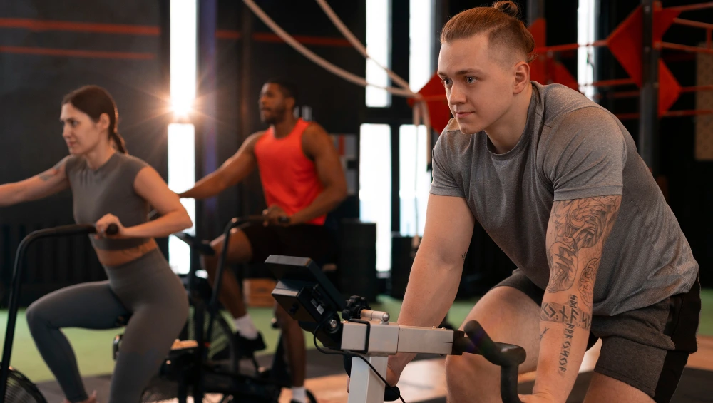 Kelsey Kane gym trainer leading energetic group fitness class at Fitness Junction with members using GHD machines and TT bikes for strength training