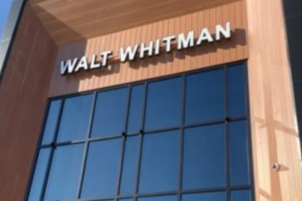 Modern exterior of the Walt Whitman Travel Plaza on the New Jersey Turnpike southbound side, showing a brick-and-glass façade, outdoor seating, and solar-lit architecture.